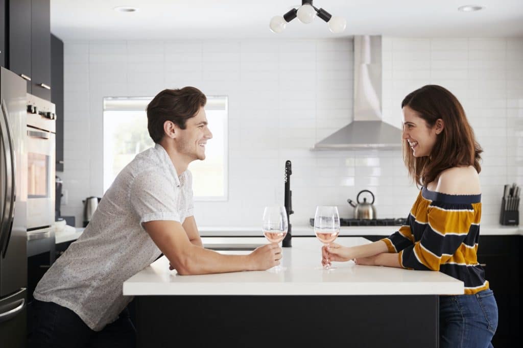 Couple Making Drinking Wine At Home Standing By Kitchen Island