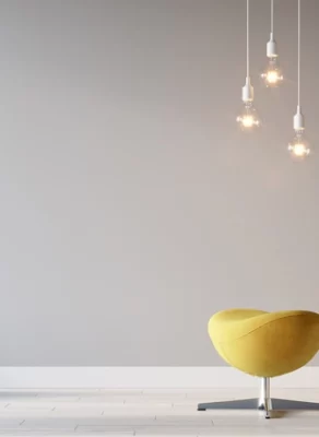 Sculpted yellow chair and ottoman with hanging lightbulbs and a potted cactus against a gray wall, showing many of the top 5 home décor trends in 2021