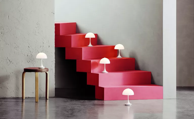 Several portable table lamps positioned on an end table, the floor, and some stairs, as part of the surprising home décor trend in 2022, as found on HomeDecorCraze