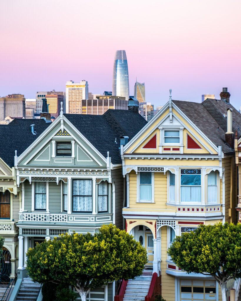San Francisco Victorian homes, one sage green, and the other yellow with white and red trim details.