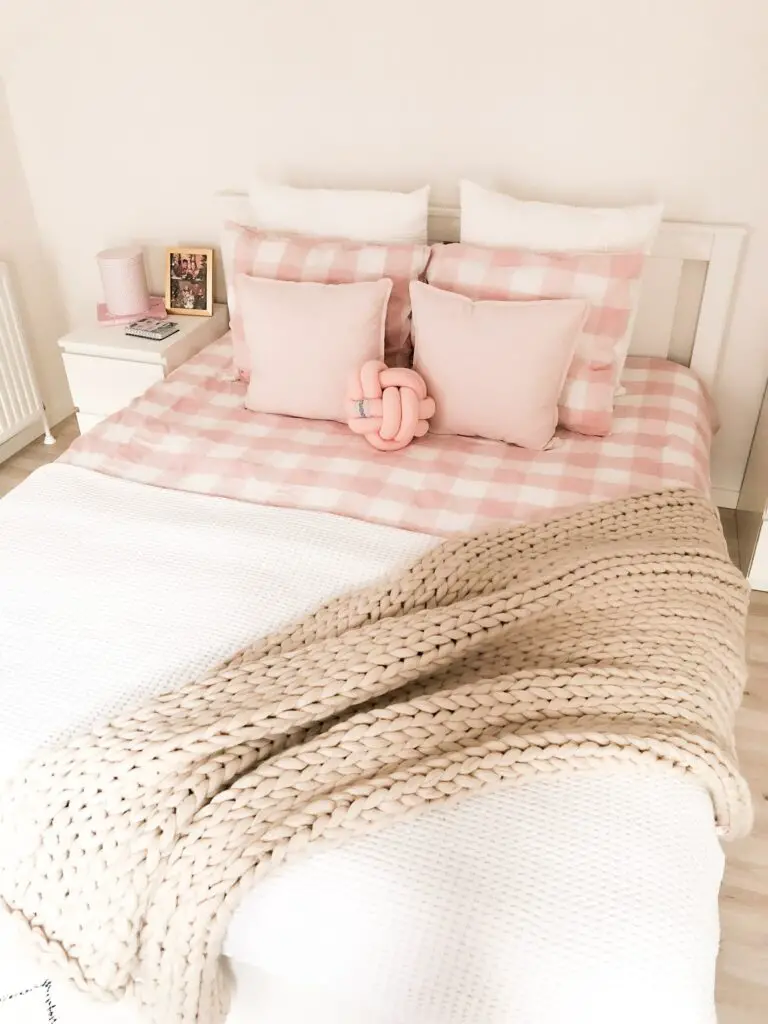 White waffle knit bedspread over pink and white gingham sheets with chunky crocheted beige throw.