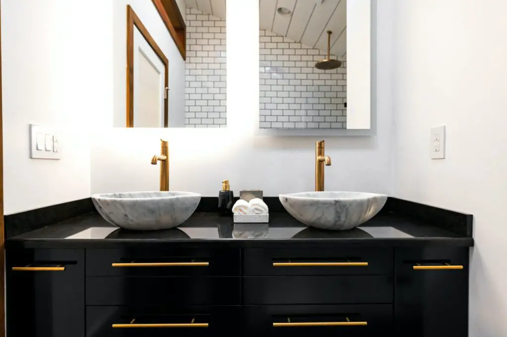 Modern black double vanity with white marble vessel sinks and brass faucets and hardware.