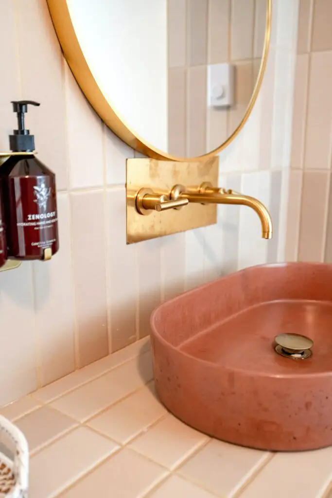 Hand-glazed gray subway tiles laid horizontally with pink stone sink and brass faucet.