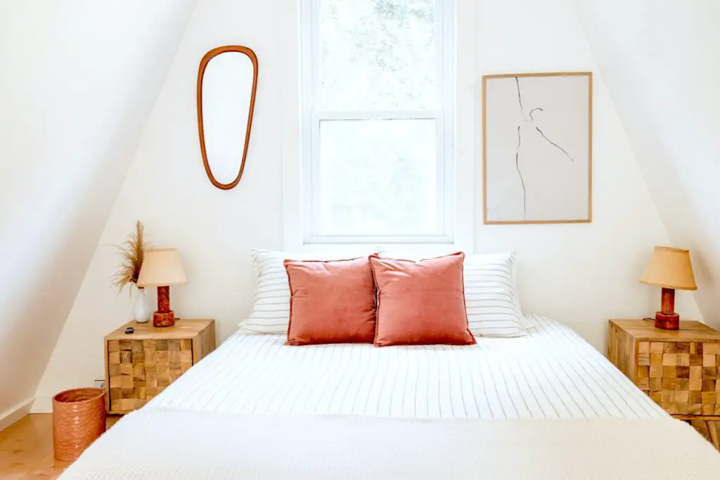 White room with bed in front of window and wood side tables. Bedding is white with faint gray stripes and pink pillows.