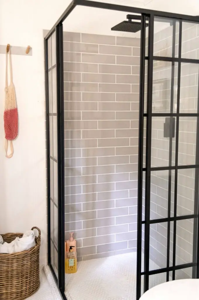 Black paned glass-enclosed shower with grey subway tiled walls.