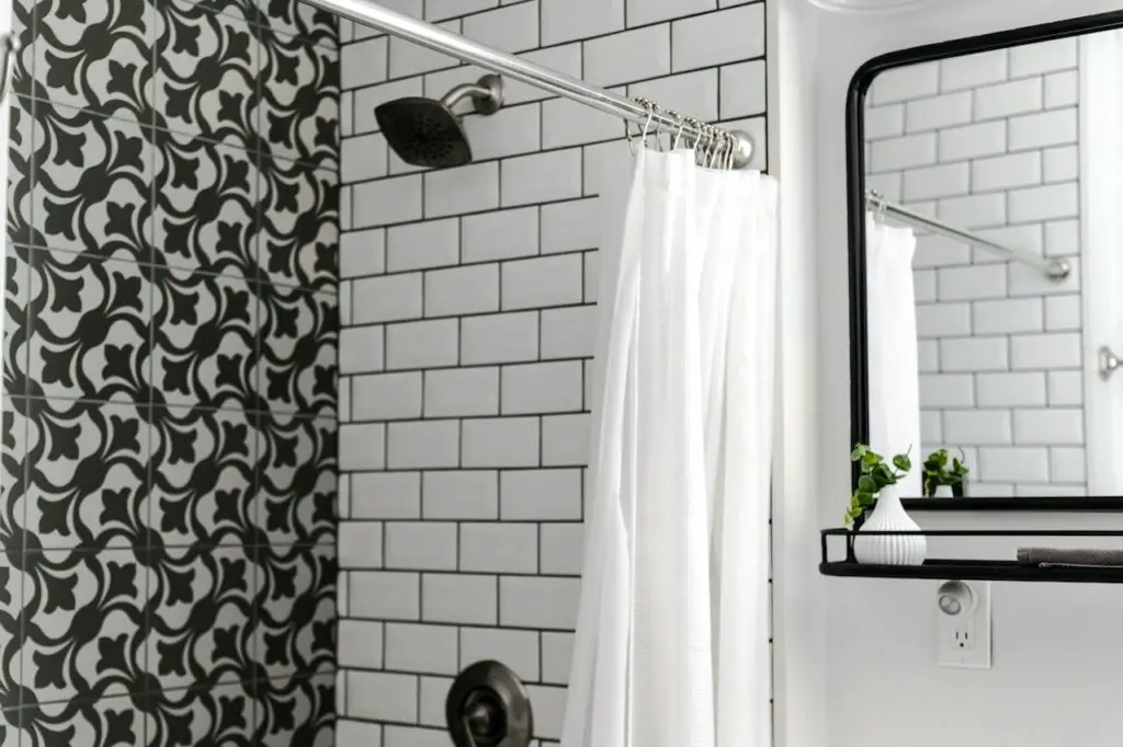 Shower with white subway tile on side wall and black-and-white cement tile on back wall.