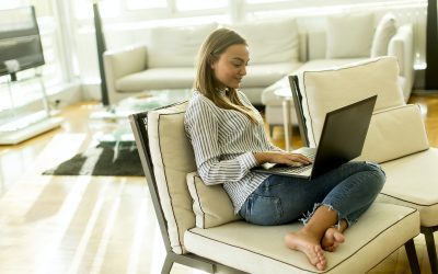 Smiling woman with a laptop lying on a sofa in her living room